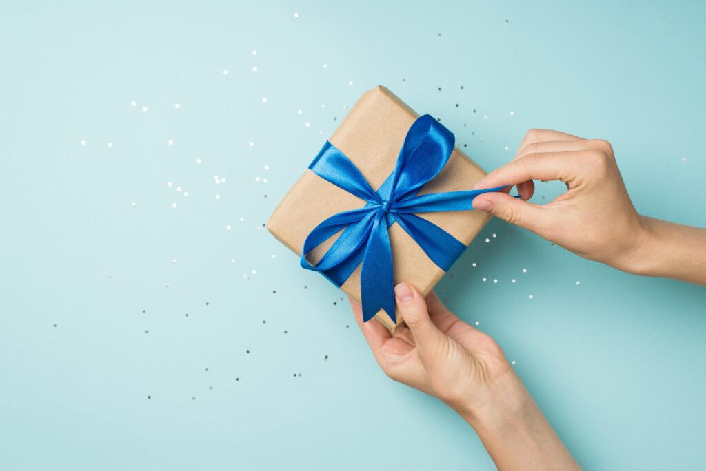 a present with a bright blue bow being unwrapped showing a pair of hands